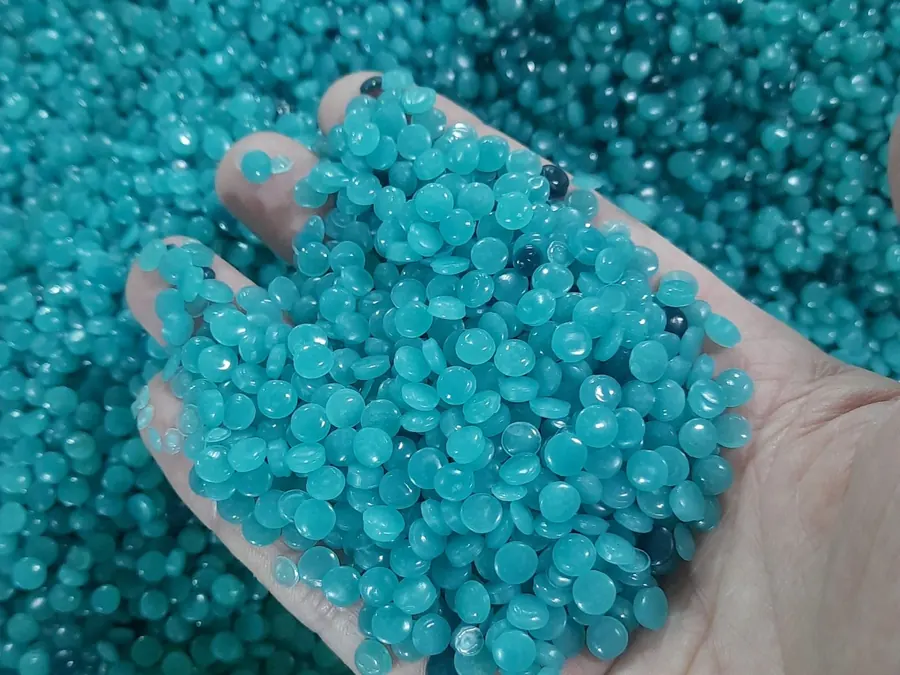 A hand holding turquoise recycled polyethylene granulate